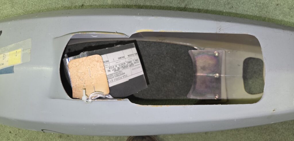 Open gray device enclosure exposing a black component with a paper label inside.