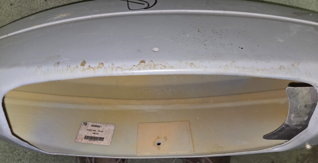 Close-up of a circular gray metal surface with brown rust streaks along the rim and a beige interior.